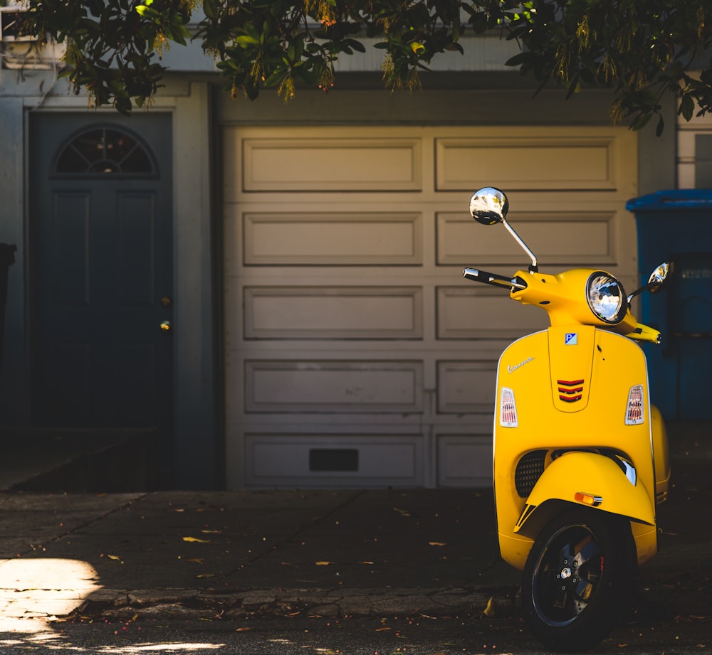 Scooter amarillo estacionado cerca de la puerta de garaje blanca
