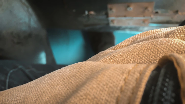 Close-up of durable fabric with burnt rust and iron gray tones layered on a machinist's workbench bathed in soft natural light.