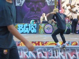 A vibrant urban scene featuring a skateboarder in motion on a graffiti-adorned skate park. Several individuals are gathered, relaxed and socializing, with a large mural depicting a stylized gorilla face in the background. The atmosphere conveys a youthful and energetic vibe.