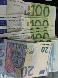 A collection of Euro banknotes, including several 100 Euro notes and one 20 Euro note. The notes are arranged in a slightly fanned-out manner, displaying the distinct designs and security features typical of European currency.