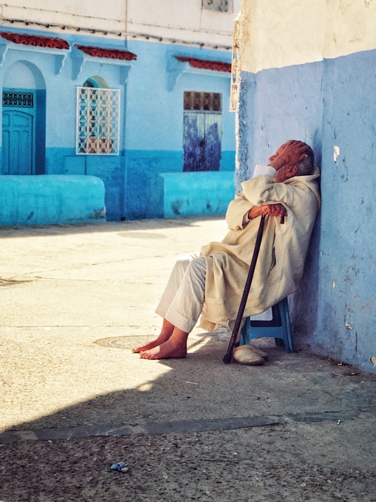 woman sitting on blue stool while holding black cane outdoor during daytime in Chefchaouen Morocco
