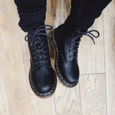 Black leather boots placed on a dark floor, highlighting their polished finish.