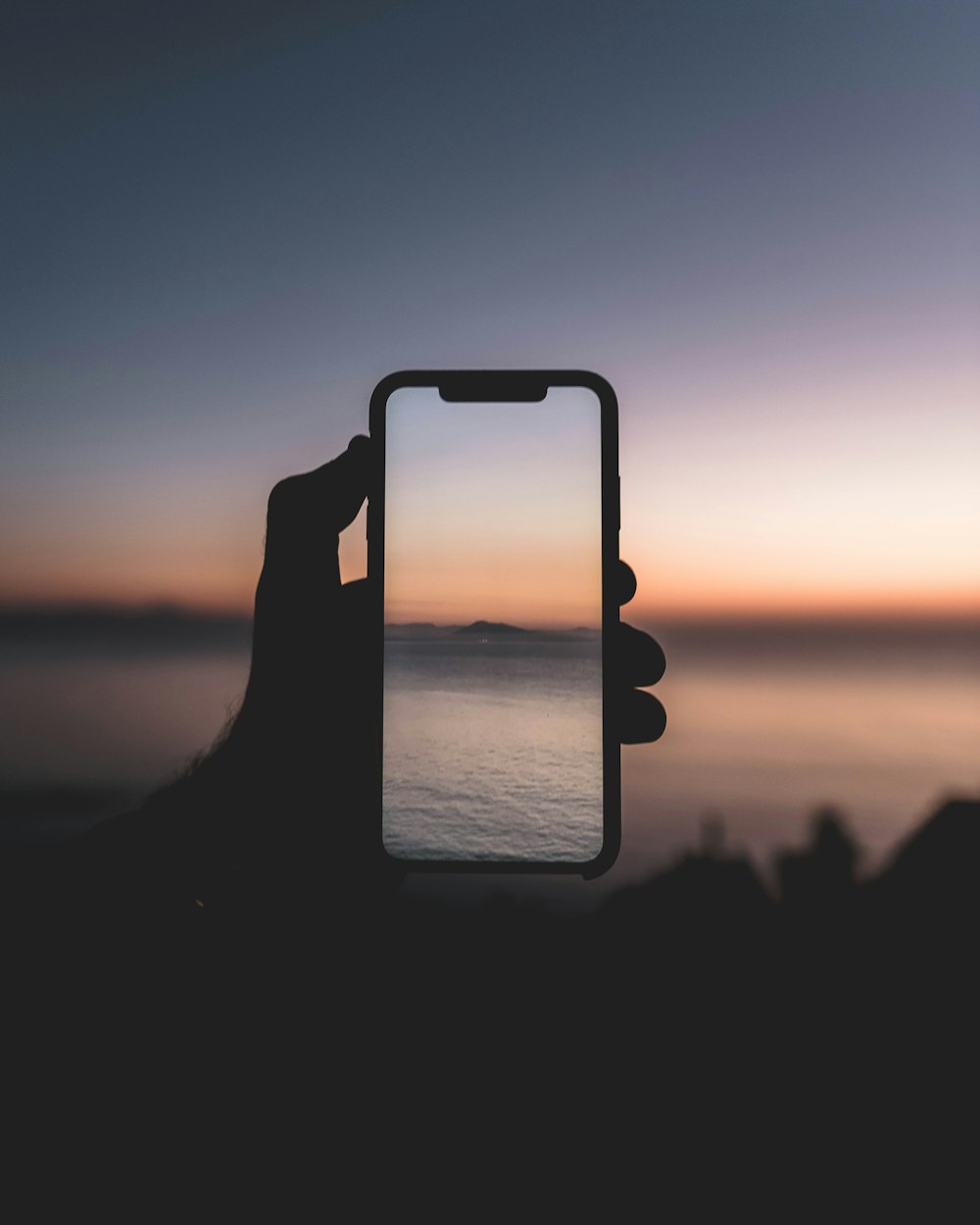 silhouette of person taking picture of body of water