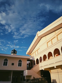 Bright yellow gradient header image of Masjid Muhajirin with sunlight filtering through stained glass windows.