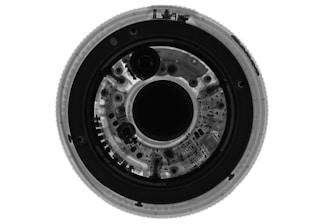 A detailed x-ray image of a circular object revealing intricate internal components and circuitry. The symmetrical arrangement shows various circular elements and patterns, likely denoting mechanical or electronic parts.