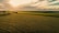 Aerial shot of a drone flying over a green agricultural field at sunset.