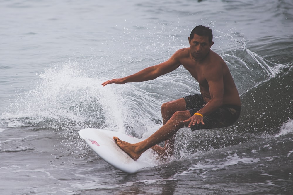 topless man surfing on body of water during daytime