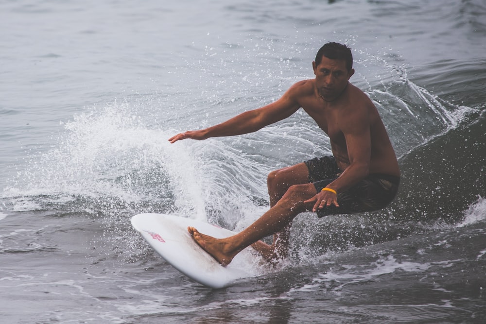 Hombre en topless surfeando en el cuerpo de agua durante el día