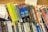 A collection of audio cassette tapes and books are arranged on a shelf. These include titles from various genres, such as mysteries, self-help, and classic literature. The tapes are stacked at different angles, creating a colorful and eclectic display with visible titles like 'Great Expectations,' 'Gulliver's Travels,' and 'The Cat Who Brought Down the House.'