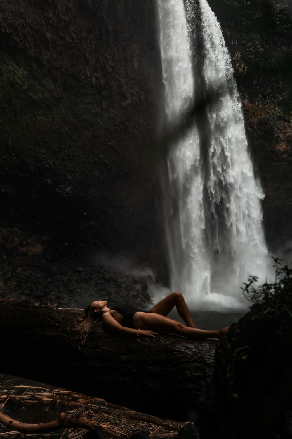 woman lying on tree log near waterfalls during daytime