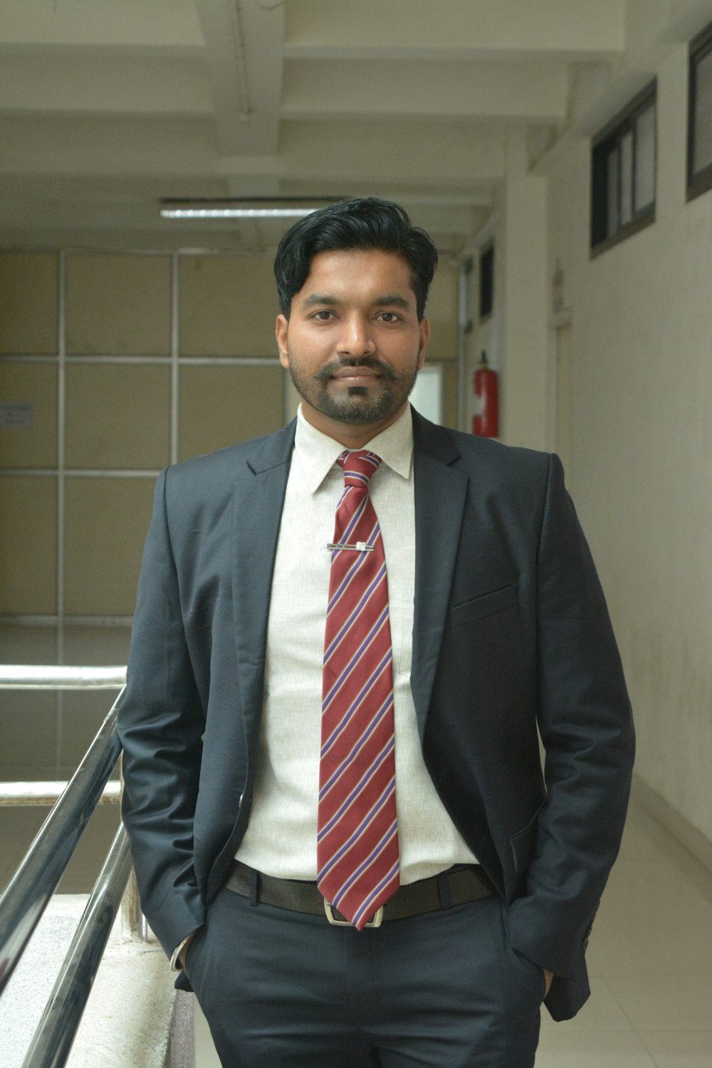 man wearing formal suit with both hands on pockets standing beside railings