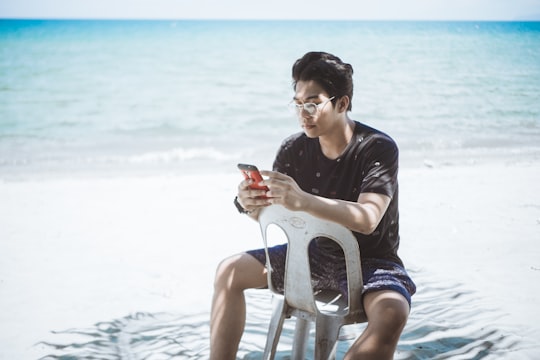man in black shirt and blue board shorts sitting on plastic chair near seashore in Cagayan De Oro City Philippines