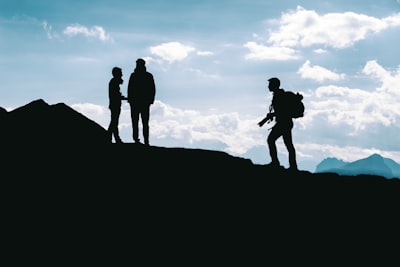 silhouette photo of three person standing on top of cliff baste teams background