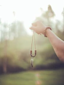 Hand adorned with layered meaningful pendants in a serene natural setting.