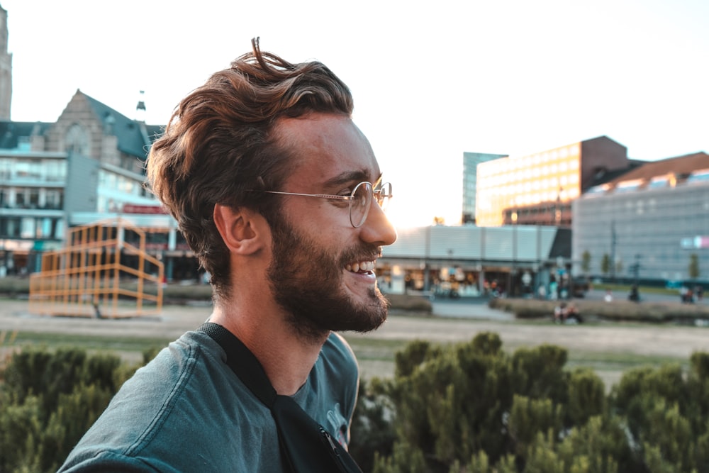 smiling man wearing eyeglasses near trees and buildings