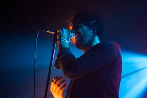 Artist laying down vocals, bathed in moody white and red spotlight against a dark backdrop.