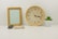 A modern table clock placed on a wooden desk beside a small plant.