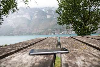 A serene outdoor scene with a tablet displaying ansudi.it, resting on a wooden bench.
