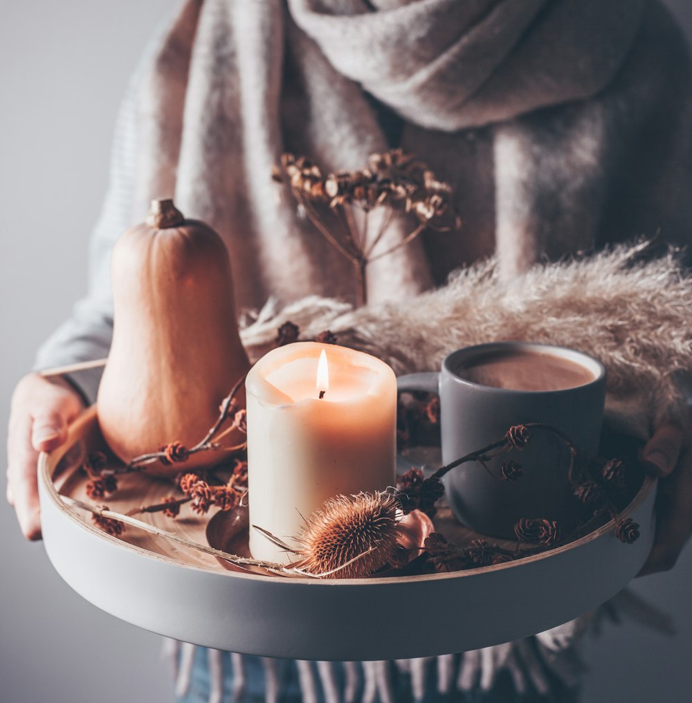 person holding beige pillar candle on gray wooden tray