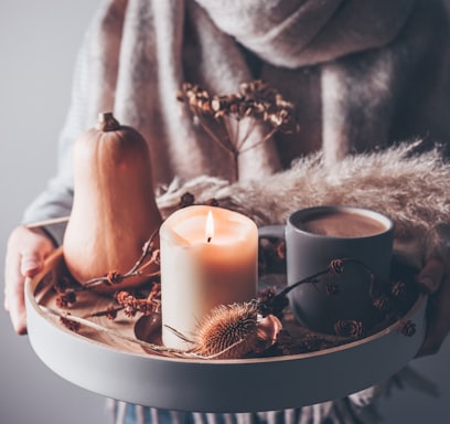 person holding beige pillar candle on gray wooden tray