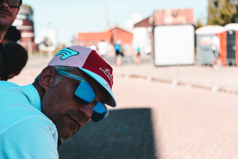 a man wearing a hat and sunglasses sitting on a bench