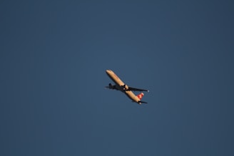 A commercial airplane is flying across a clear blue sky with a visible logo on the tail fin. The aircraft is illuminated by natural light, suggesting it might be flying during the day.