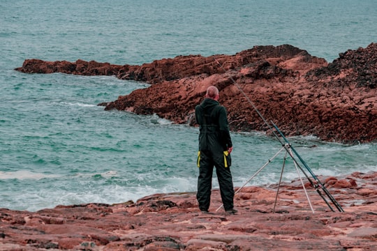 man standing in front of fishing rod on shore in Bude United Kingdom