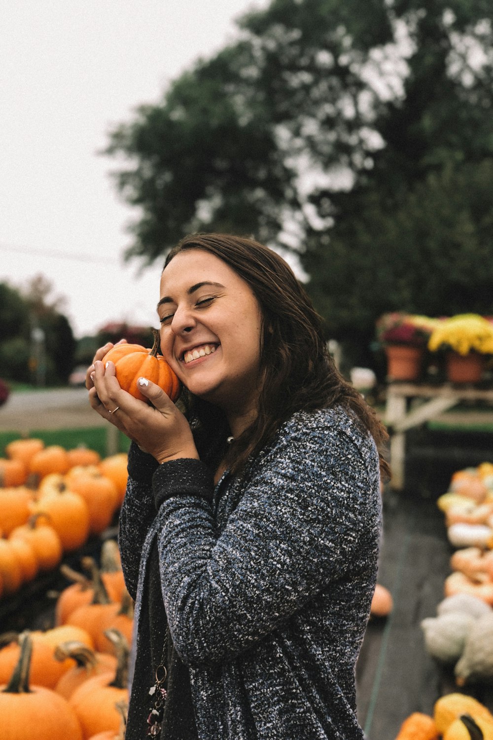 femme tenant une citrouille orange à l’extérieur près d’un arbre à feuilles vertes sous le ciel blanc pendant la journée