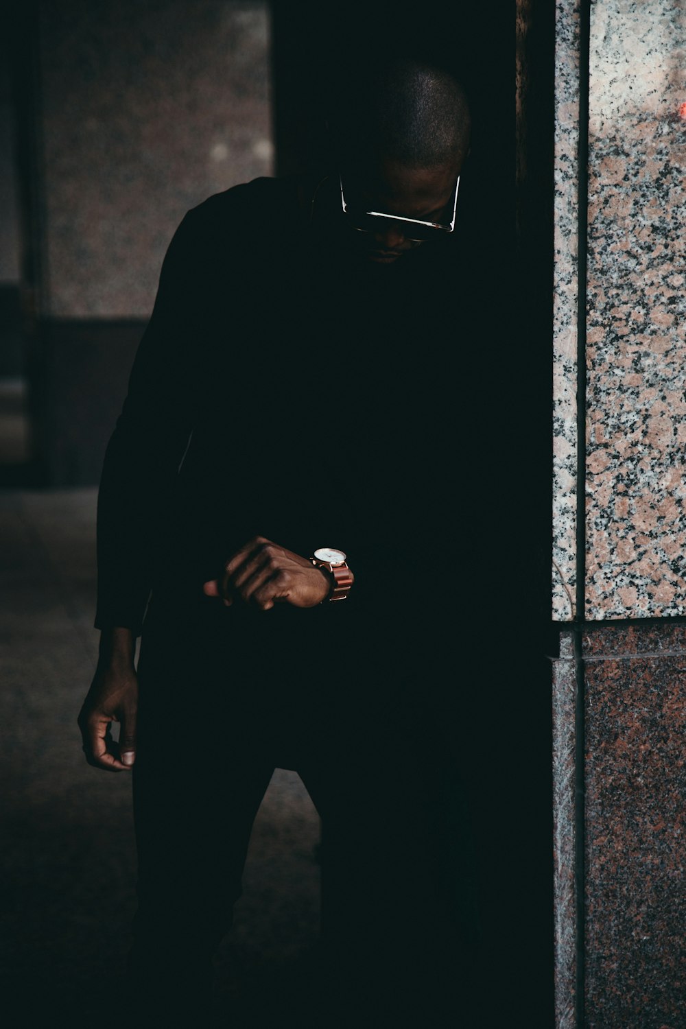 man leaning on wall staring his watch