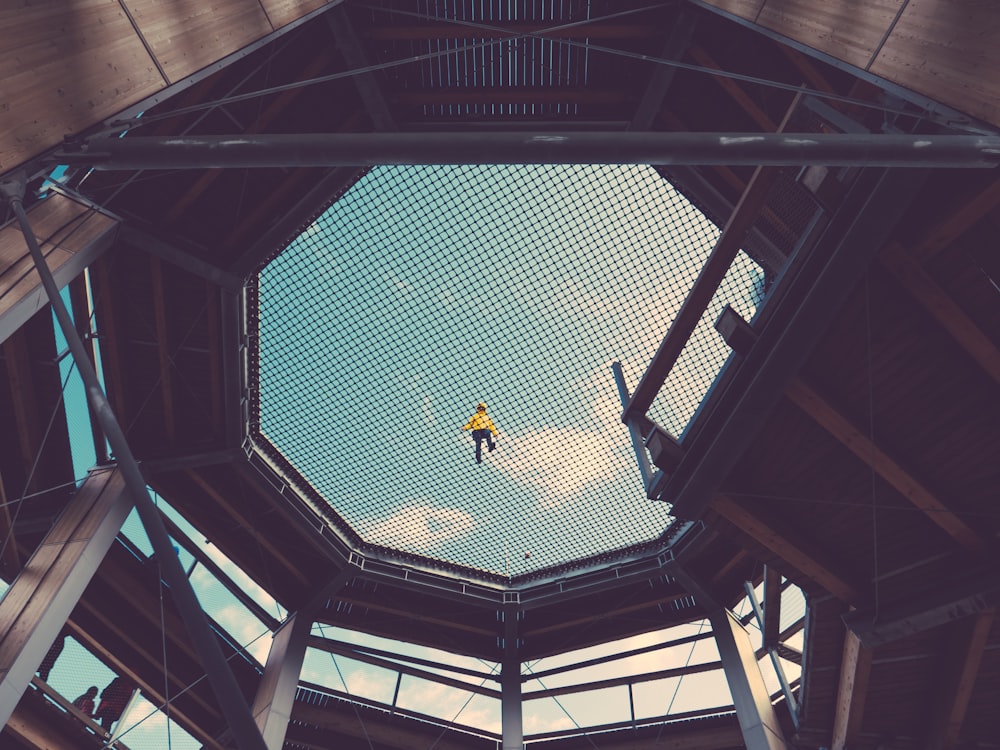 a man in a yellow shirt is suspended from a high ceiling