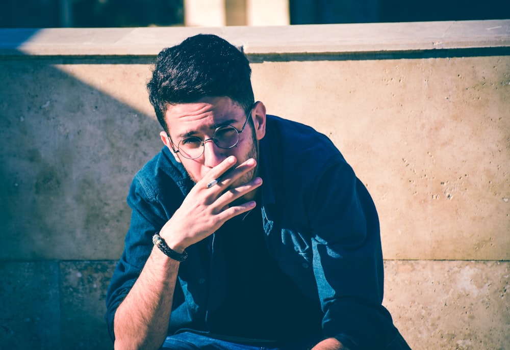 person wearing blue shirt sitting in front of concrete wall