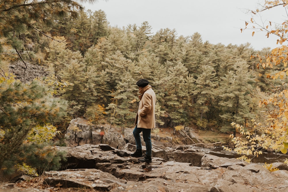 man standing on rocky cliff surrounded with trees during daylight