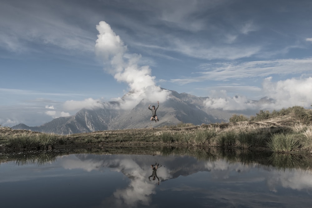 man jumps toward water under blue sky