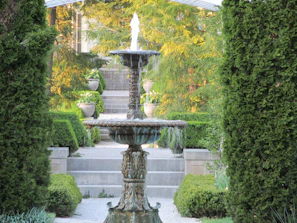 A beautifully crafted polyester garden fountain surrounded by lush greenery.