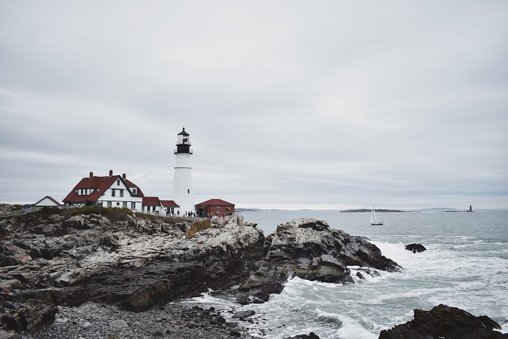 white and red house near lighthouse viewing sea