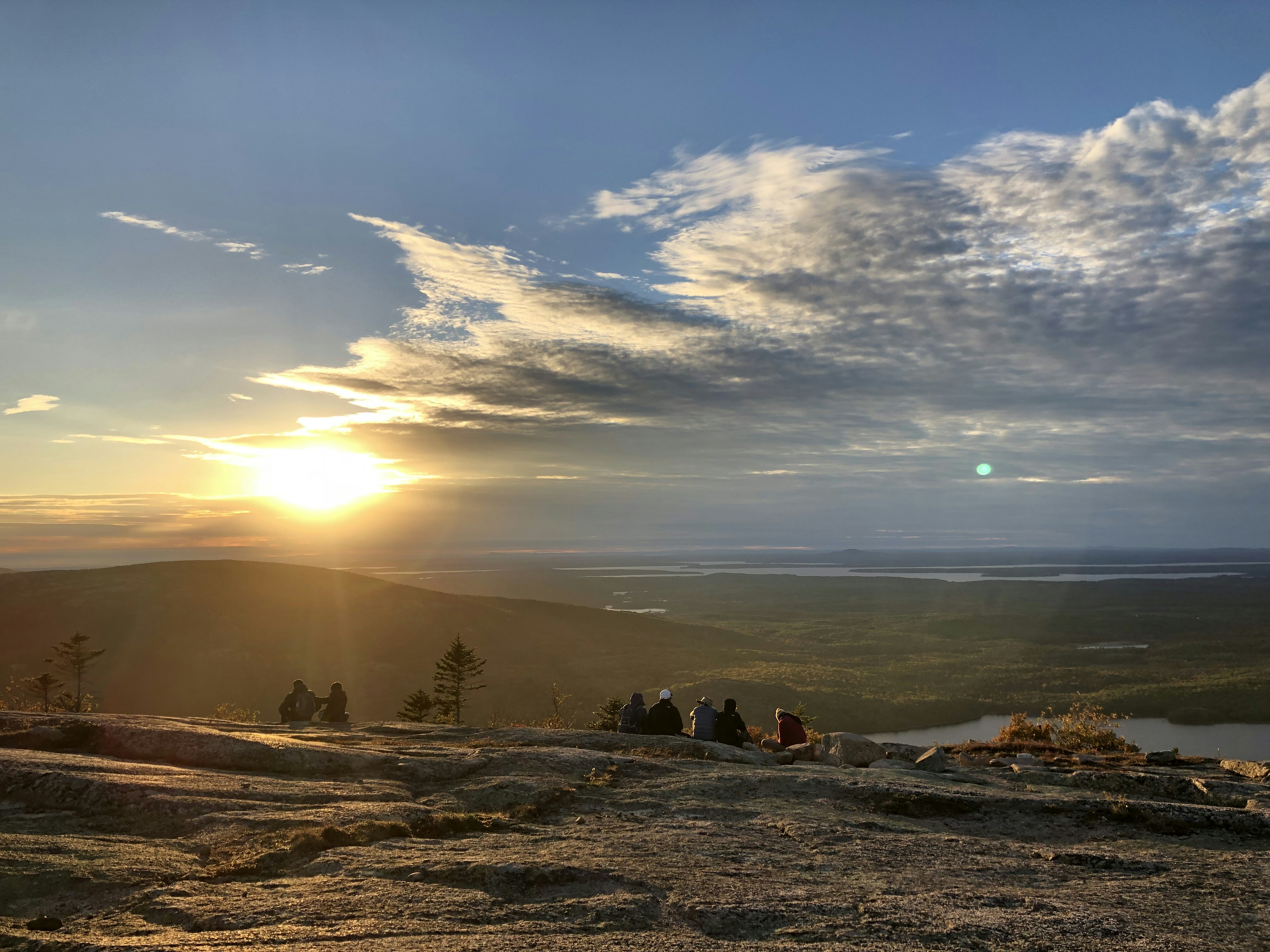 people sitting on cliff facing mountains under cloudy sky