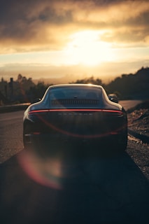 Side view of a sleek car mid-flip over a sharp platform jump under a vibrant sunset sky