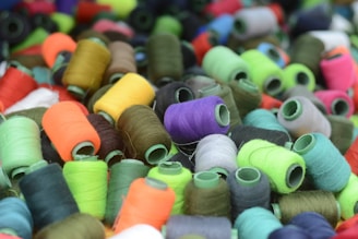A collection of colorful thread spools tightly packed together, featuring a wide range of vibrant colors. The threads vary in shades including green, red, purple, and brown, creating a lively and diverse visual display.