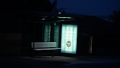 A dimly lit bus stop bench is illuminated by an advertisement panel displaying an internet service promotion. The surrounding area is dark, with the advertisement text prominently visible.