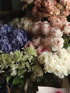 A beautiful arrangement of flowers featuring pink and white roses, purple hydrangeas, and white blossoms with green foliage.