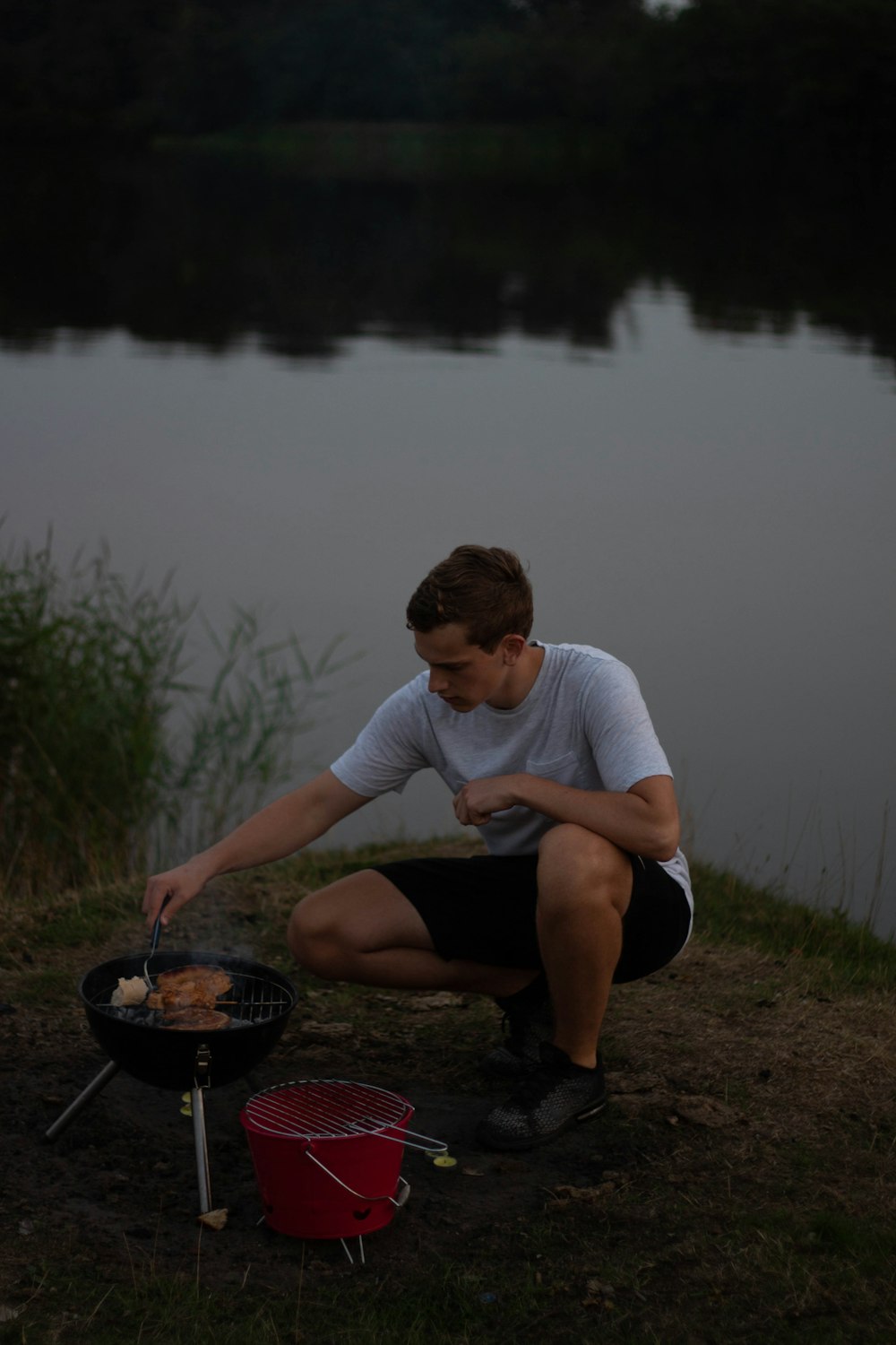 man grilling on charcoal grill near body of water