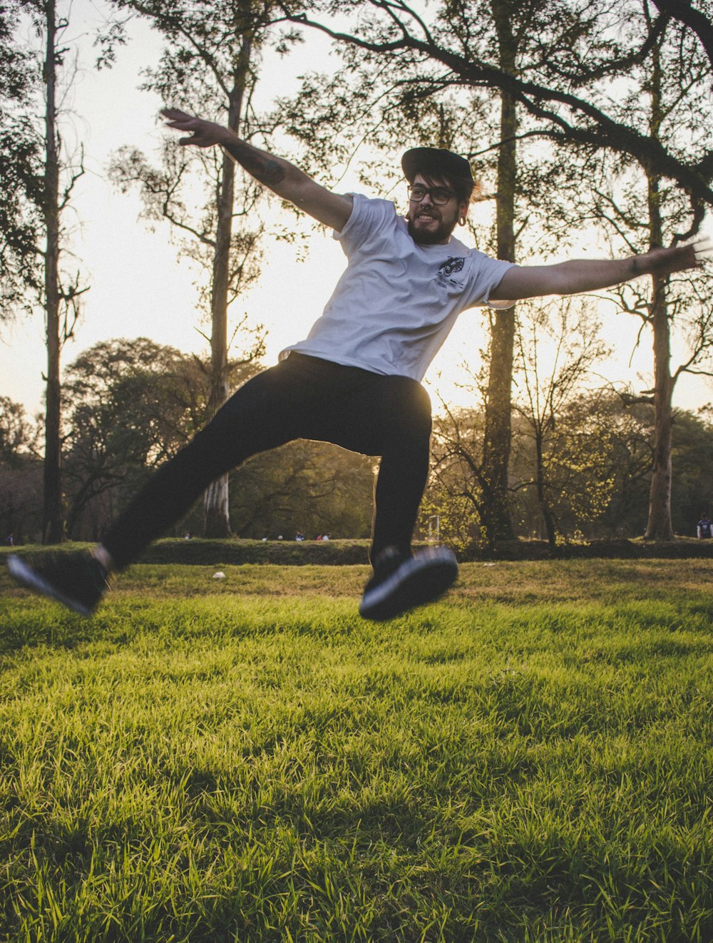 man jumping above green grass with trees behind during golden hour
