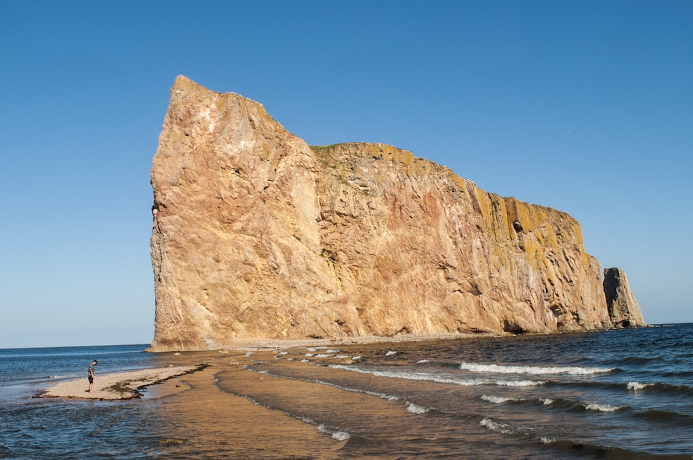 a person standing on a beach next to a large rock