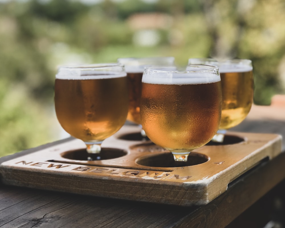 four wine glasses filled with liquid on wooden tray selective focus photography