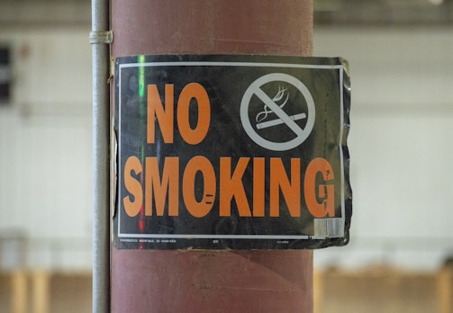 A sign attached to a pole with the words 'NO SMOKING' in bold orange letters and a graphic of a cigarette crossed out.