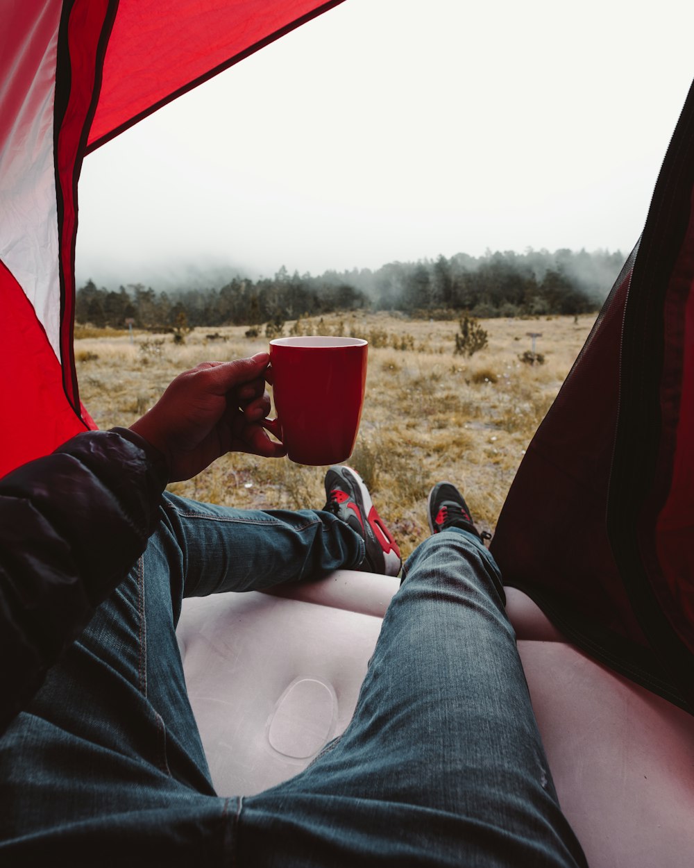 man resting inside tent holding red mug