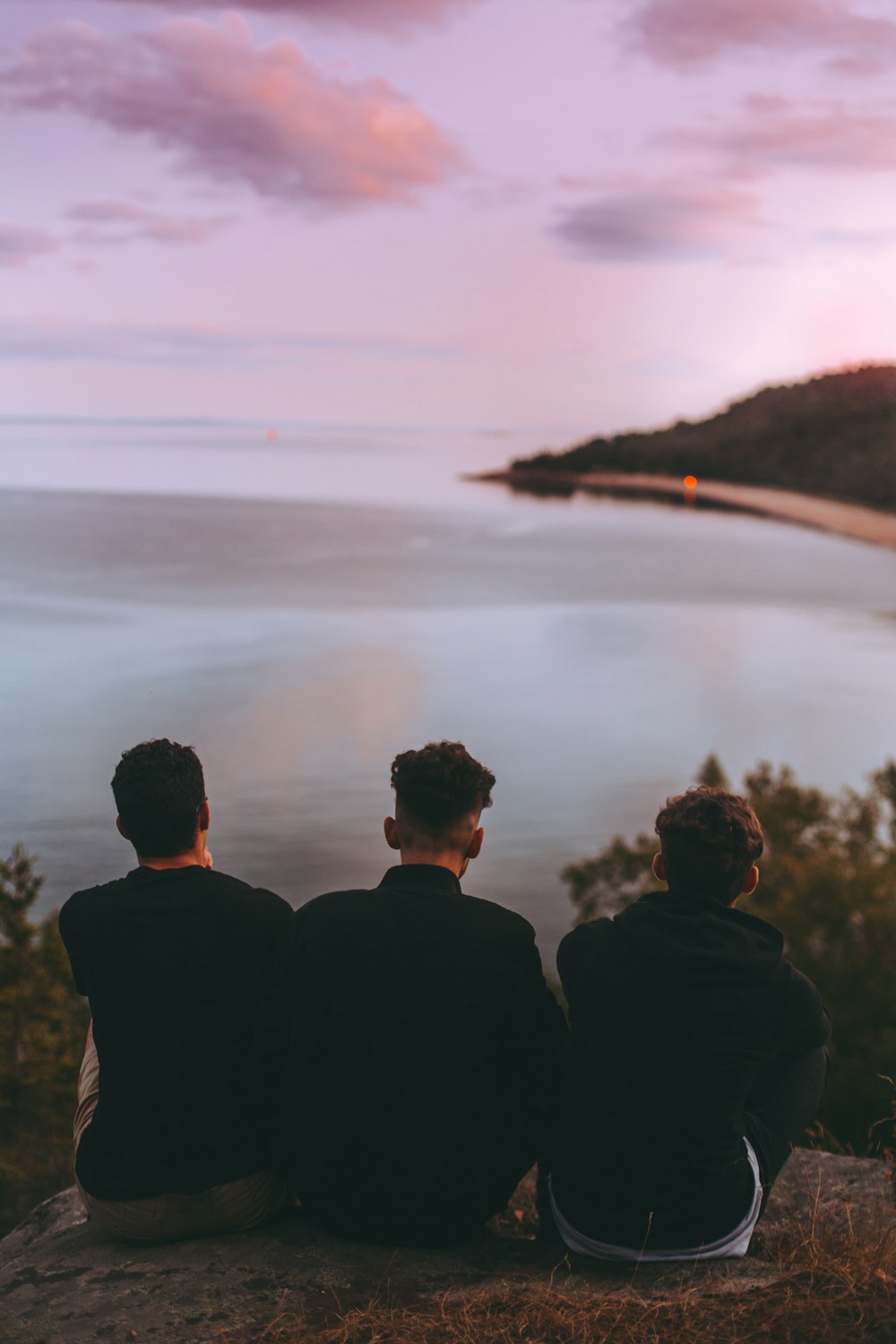 three men sitting near body of water