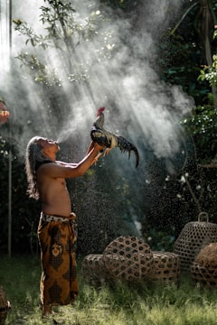 man raising rooster while blowing smoke during daytime