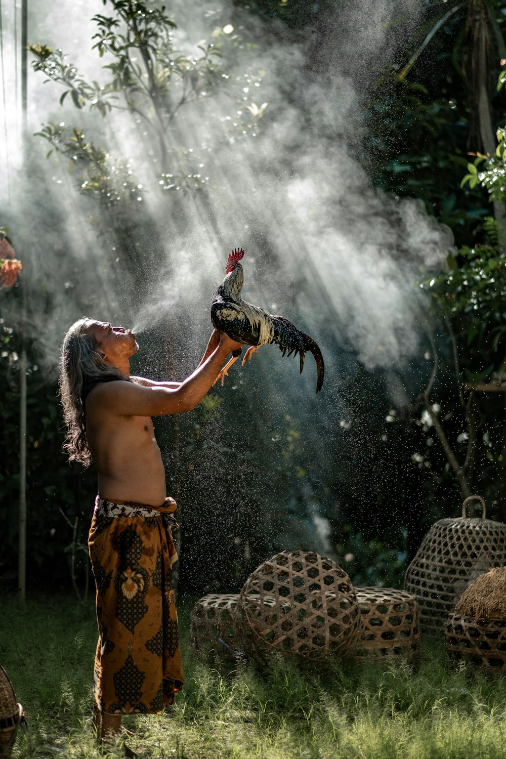 man raising rooster while blowing smoke during daytime