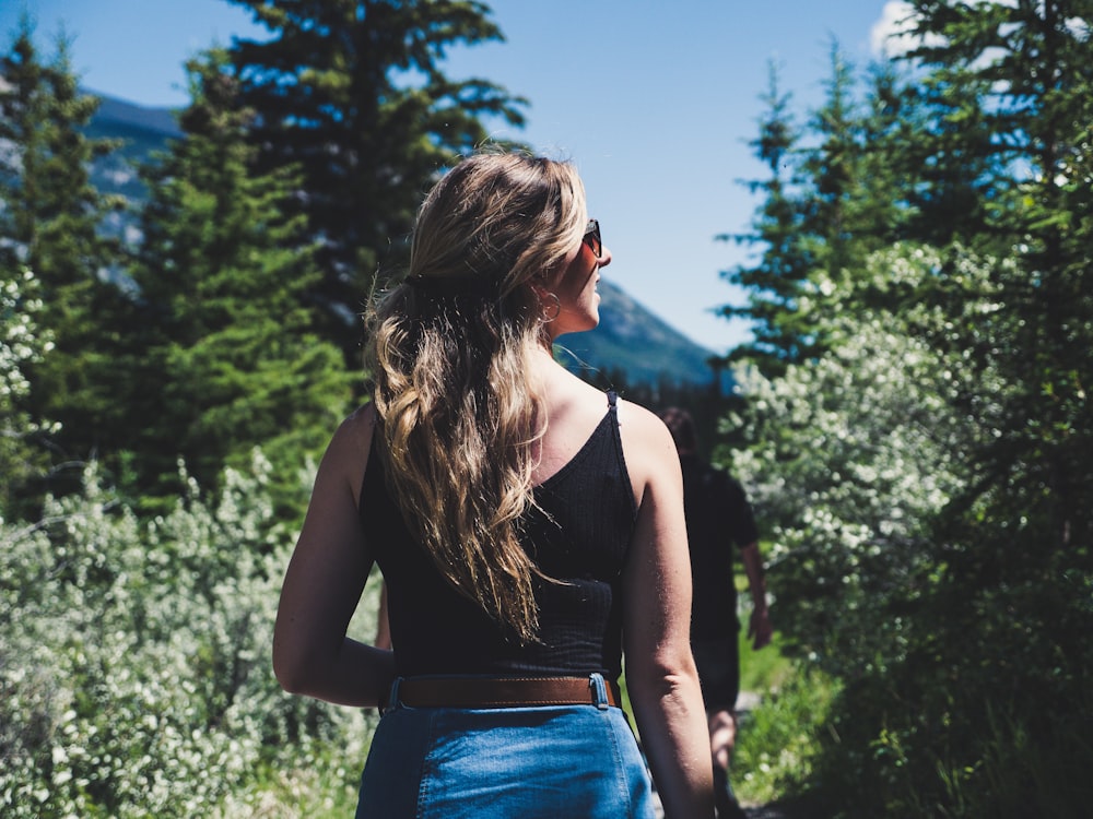 woman wearing black spaghetti strap crop top standing in front of trees while looking left side during daytime